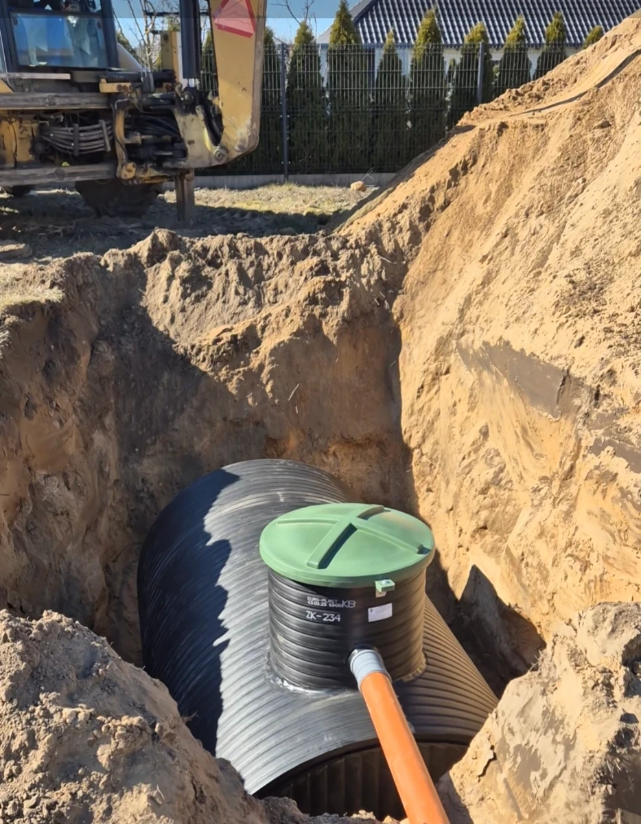 Instalacja zbiornika na deszczówkę w wykopie – plastikowy zbiornik z zielonym włazem i rurą odpływową