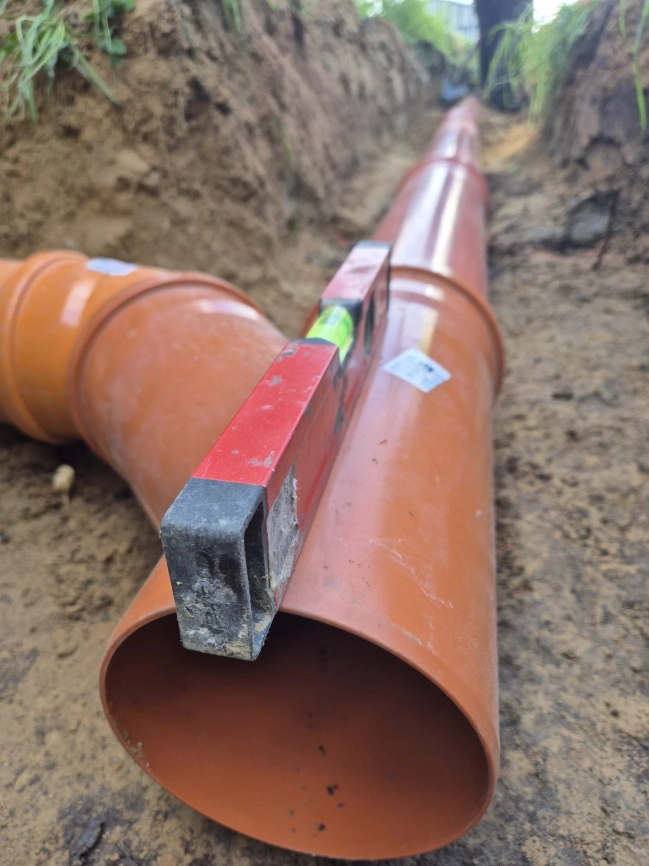 Układanie rur kanalizacyjnych w wykopie pod przydomową oczyszczalnię ścieków