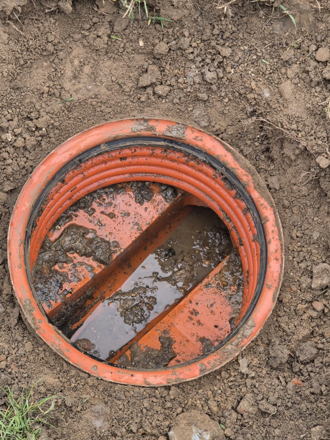 Otwarta studnia rewizyjna systemu wodno-ściekowego z plastikową obudową i zastoiną wody