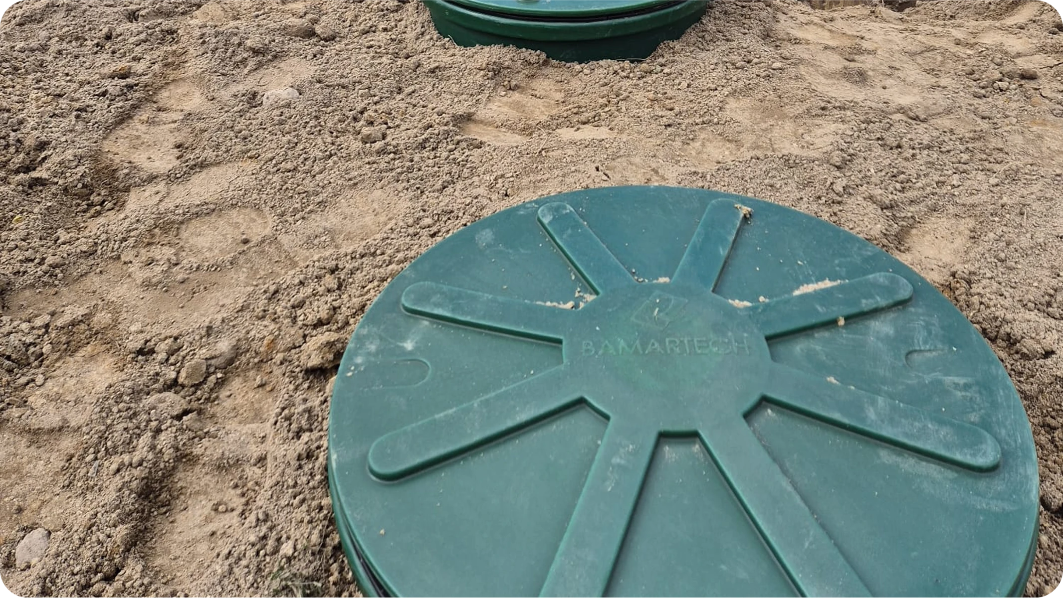 Dwie zielone pokrywy szamba ekologicznego osadzone w gruncie na przygotowanym terenie budowy