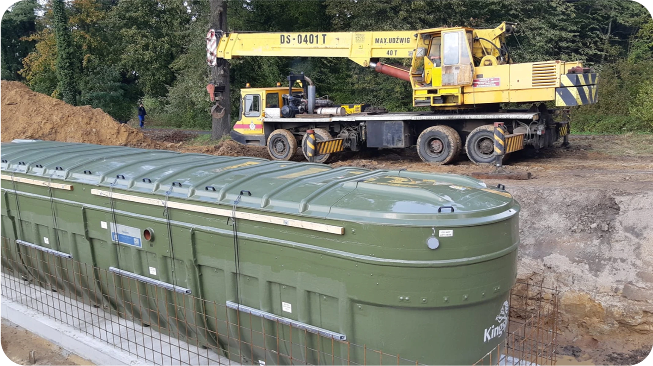 Przydomowa oczyszczalnia ścieków w trakcie montażu – zielony zbiornik w wykopie i dźwig na placu budowy