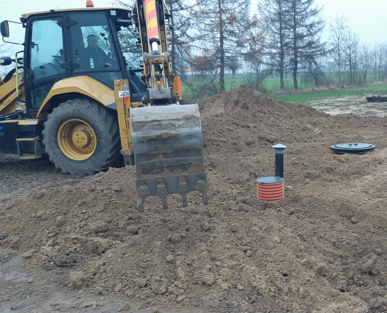 Koparka wykonuje wykop wokół instalowanego włazu przydomowej oczyszczalni ścieków