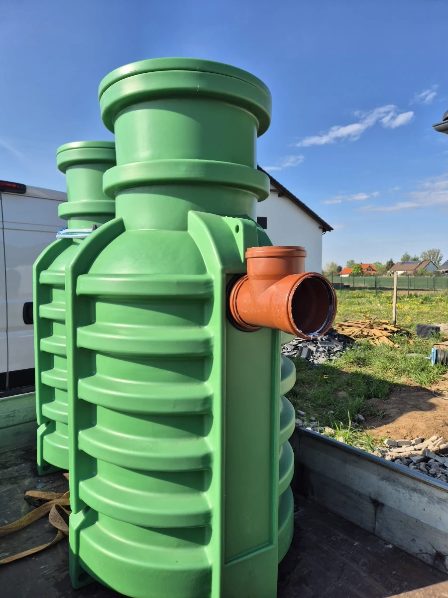 Zielony plastikowy zbiornik z pomarańczowym przyłączem, element systemu Przydomowa oczyszczalnia ścieków, gotowy do montażu w terenie